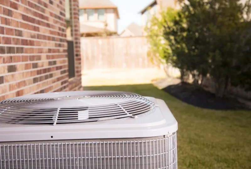 Outdoor central air conditioning condenser beside a brick home